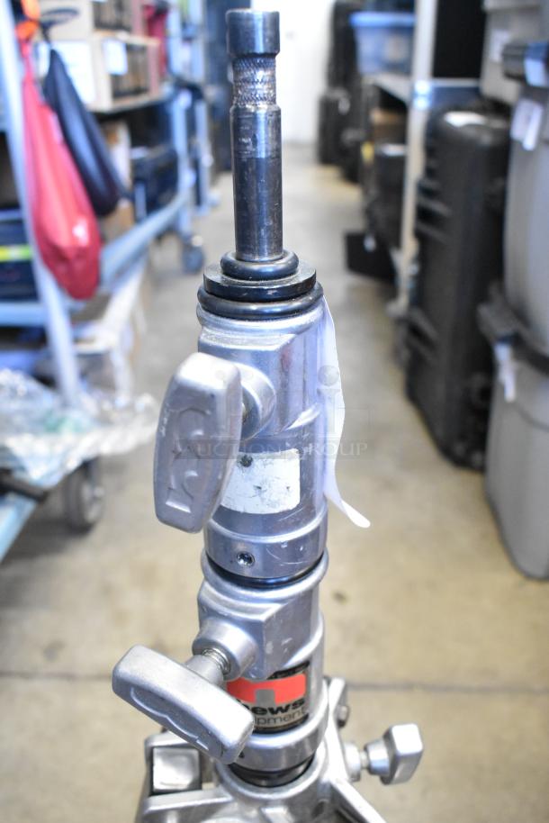 Matthews Tripod with adjustable metal knobs, visible brand label, in good condition, stored in a warehouse setting.