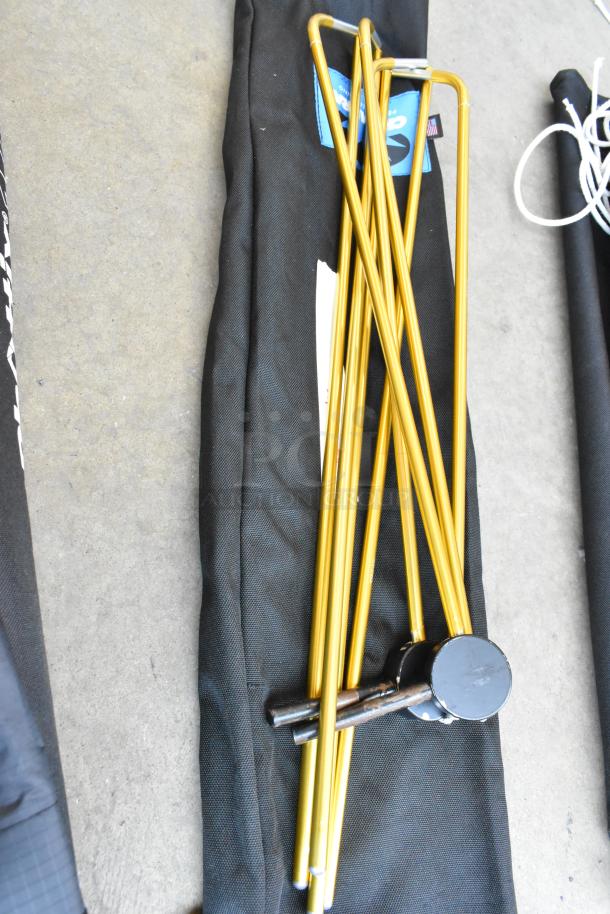 Golden fabric holder with lighting gear, featuring metal rods, on black carrying case. Includes attached identification tags.