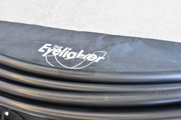 Umbrella/light gear with "The Eyelighter" branded fabric holder, featuring black curved support rods, in excellent condition.