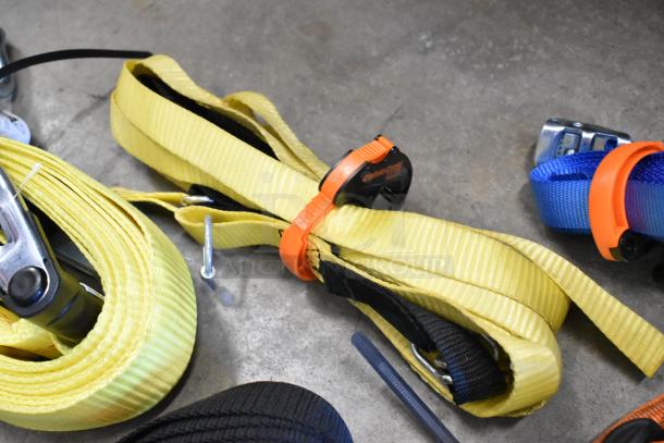 Lot of various colored ratchet straps in a poly bin, featuring yellow, blue, and black webbing, equipped with metal hooks and tensioners, for securing loads efficiently.