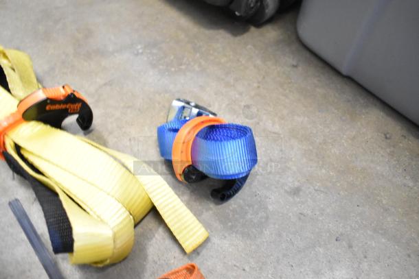 Lot of ratchet straps in poly bin, includes yellow, blue, and black straps. Features branded buckle and wrist strap.