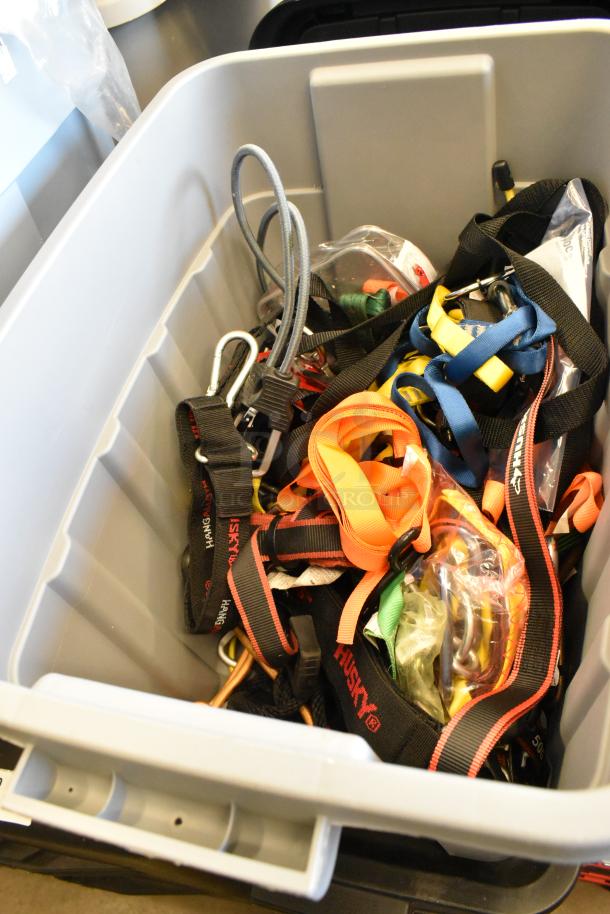 Lot of assorted ratchet straps in various colors stored in a gray poly bin. Some straps branded Husky.