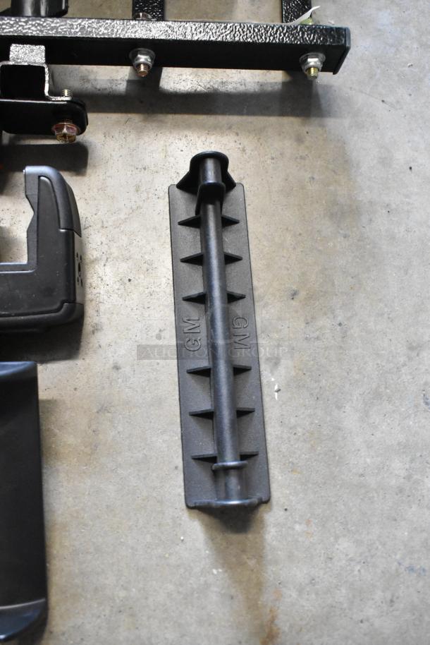 Lot of various metal and plastic items including a black piece marked with "GM" on a gray textured surface.