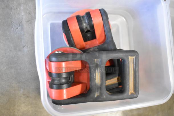 Poly bin containing various red and black parts, possibly caster wheels, in used condition.