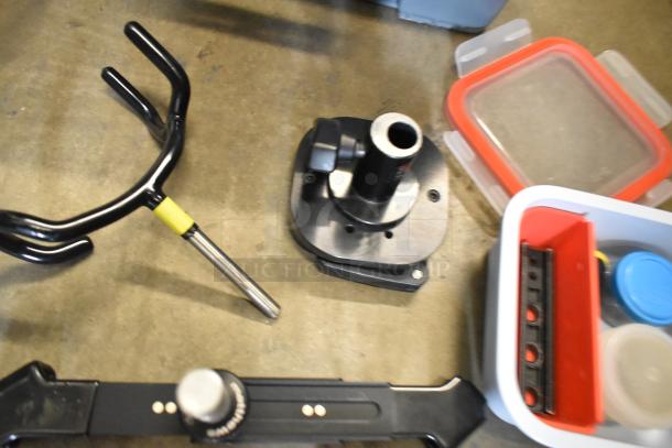 Lot of various parts and pieces in a poly bin, includes a black metal bracket, a plastic base, sealed containers, all in used condition.