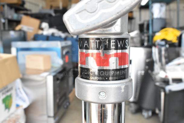 Matthews Studio Equipment tripod on casters, in used condition. Label indicates brand and contact info: Burbank, CA, 818-843-6715.