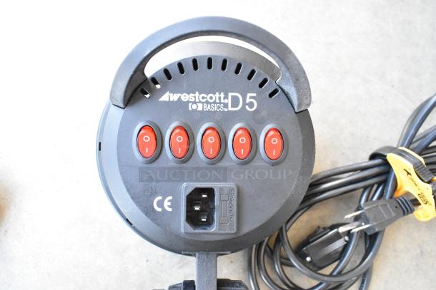 Westcott Basics D5 light with power switches, cables, and plug on concrete surface; part of lighting equipment lot.