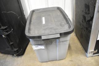 Gray poly bin with black lid labeled "329," containing various items including shoulder straps. Condition appears used.