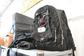 Four various soft bags displayed on a shelf, including a black backpack with multiple zippers and a tag labeled "333."
