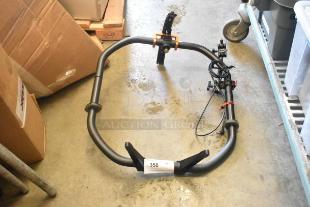 Black metal frame, possibly a mounting component, on warehouse floor. Includes wiring and a label marked "358 QTY".