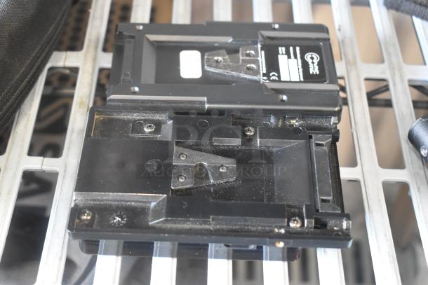 V Mount to Gold Mount Adapter, black with visible mounting screws, used condition, placed on metal grate surface.