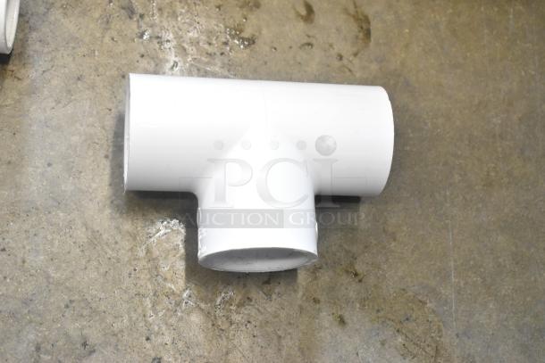 PVC pipe T-fitting on concrete floor, part of a mixed lot in poly bin, appears in good condition.