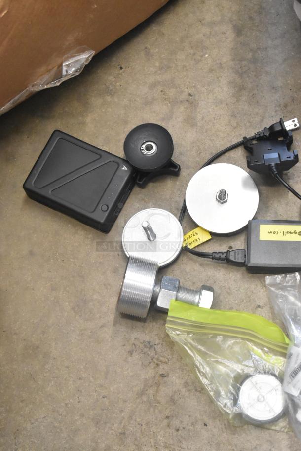 Lot of various hardware items in poly bin, including black device with cord, metal rollers, and sealed components. Labels visible.