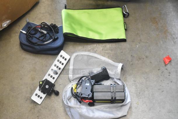 Various hardware items in a poly bin, including a green pouch, cables, a metal plate, and a black attachment.