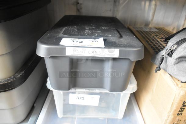 Poly bin labeled "HDMI Cables," containing various items, with visible auction tags numbered 372 and 373, in storage setting.