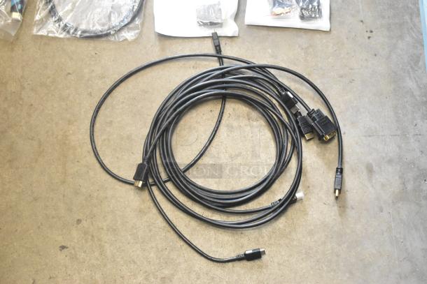 Lot of various cables, including HDMI and USB, coiled on concrete floor. Part of an assorted item collection in poly bin.