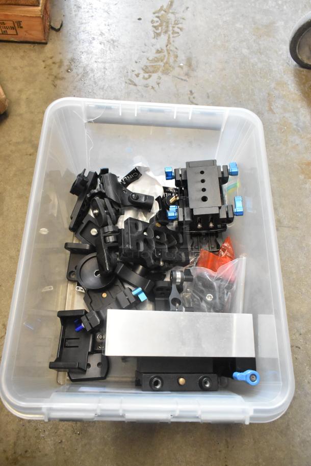 Poly bin with assorted camera attachment gear, various black metal brackets, mounts, and hardware. Good condition.