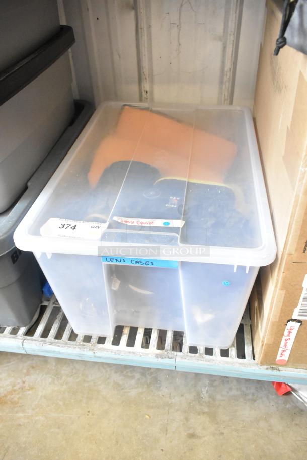Clear poly bin labeled "Camera Equip." and "Lens Cases," containing camera equipment and lenses. SE374 tag visible.