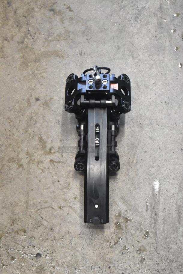 Black mechanical unit on concrete surface, featuring a sturdy metal frame with visible bolts and hinges; no visible bag in image.