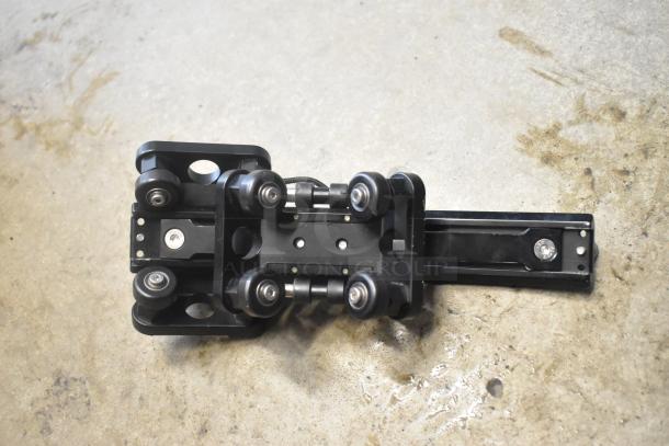 Black mechanical unit with multiple wheels, featuring sturdy metal construction. No visible labels or tags. Condition appears good.