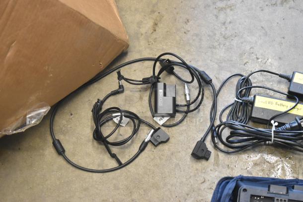 Cables and chargers labeled "Small HD Battery Charger" on concrete floor near cardboard box. No monitor visible.