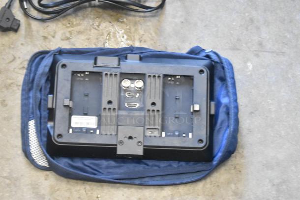 Small HD Monitor with dual HDMI ports and battery slots; appears in blue fabric case; power cables included.