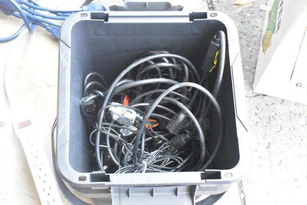 Poly bin containing a variety of cords and adapters. Items are coiled and appear used. Ideal for electronics setup.