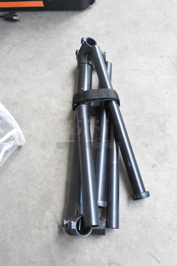 Lot of various items including folded black Movi handles, secured with a strap, on a concrete floor.
