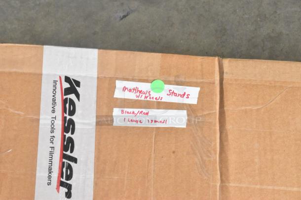 Cardboard box labeled "Matthews Stands." Contains one large and one small black/red stand with wheels. Packaging shows "Kessler" branding.