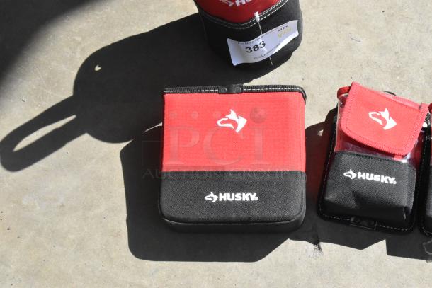 Four red and black Husky tool bags on concrete. New condition with visible logos. Auction lot tag: "383."