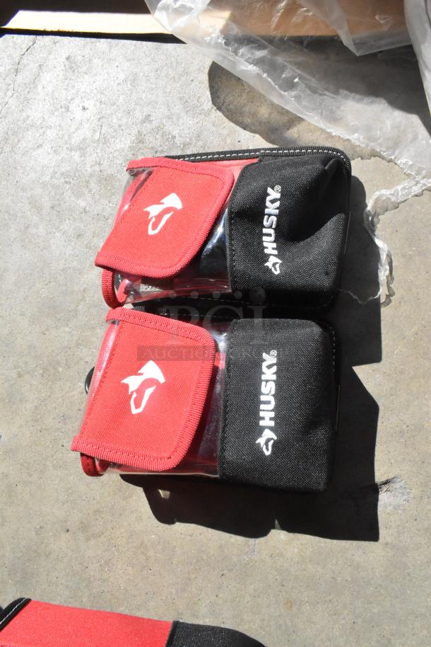 Four Husky tool bags, red and black with logo, in new condition. Snap closure and compact design.