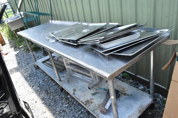 Stainless steel table with under shelf, holding metal pans and dunnage racks, on casters, outdoor condition.