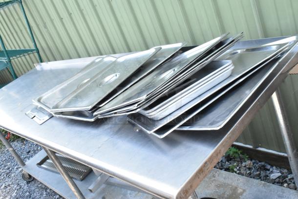 Stainless steel table with under shelf, includes dunnage racks and metal pans. Visible wear, ideal for kitchen use.