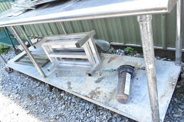 Stainless steel table with under shelf, includes dunnage racks and metal pans, on wheels; visible weathering.