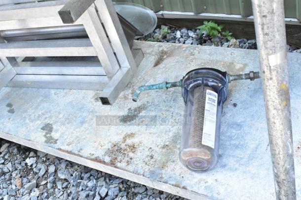 Stainless steel table with under shelf, includes dunnage racks and metal pans, seen with water filter and pipe fitting.