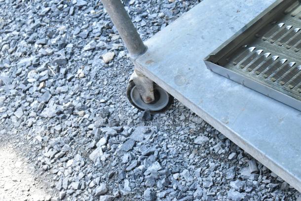 Stainless steel table with under shelf, includes dunnage racks and metal pans. Visible caster wheel, outdoor use condition.