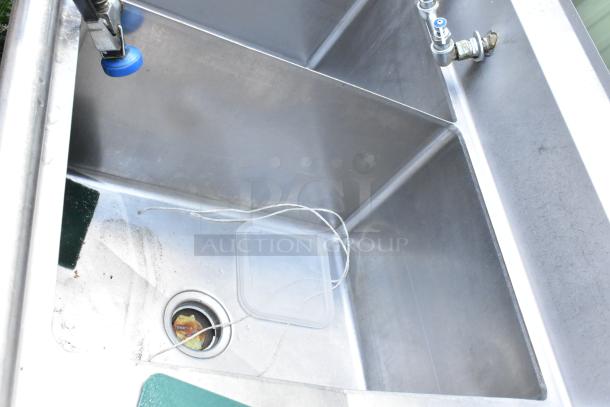 Stainless steel 3 bay sink with dual drain boards, handles, and spray nozzle attachment, showing clean condition.