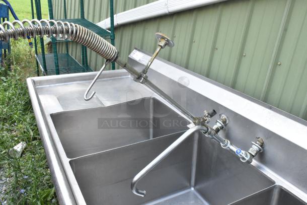 Stainless steel 3 bay sink with dual drain boards, handles, and spray nozzle attachment. Ideal for commercial use.