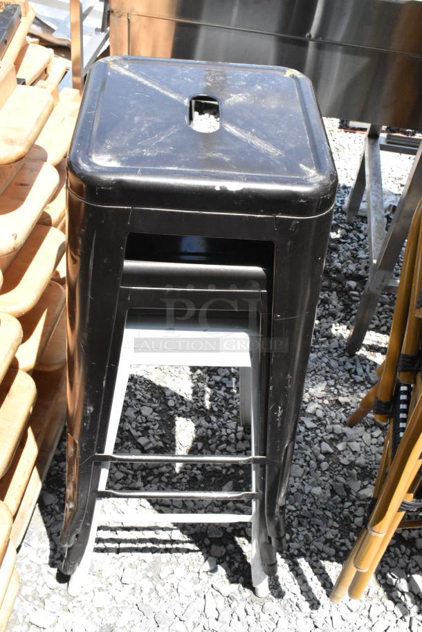 Set of 8 black metal Tolix style stools stacked, showing a durable industrial design with visible wear marks.