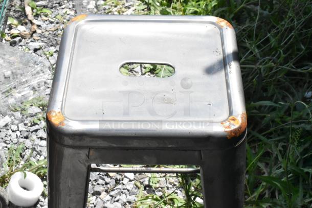 8 metal Tolix style stools, industrial design, visible rust on edges, silver finish, stackable, weathered condition.