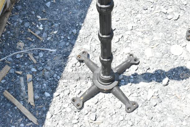 Metal table base with four-point design, suitable for outdoor use. Rust spots visible, indicating wear.