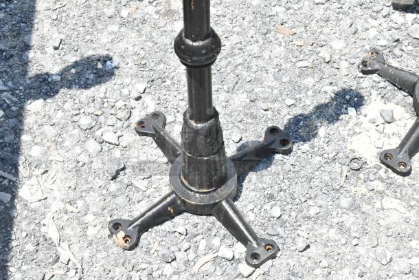 Black metal table base on gravel; one of seven table bases in the auction, with rust spots visible.