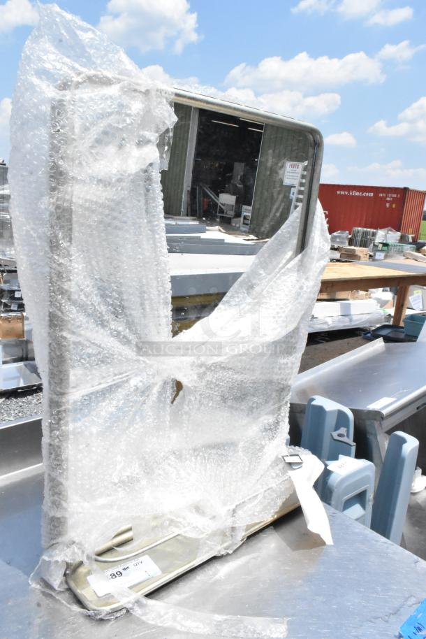 Rectangular mirror wrapped in bubble wrap, partially exposed. Metal frame visible, placed on industrial surface.