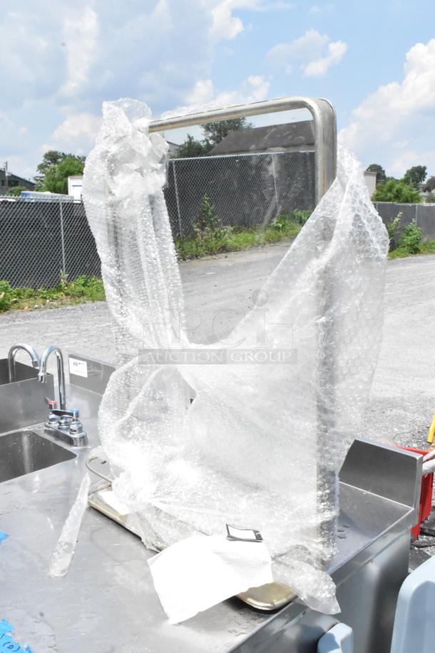 Reflective metal-framed mirror wrapped in protective bubble wrap, showing partial outdoor setting.