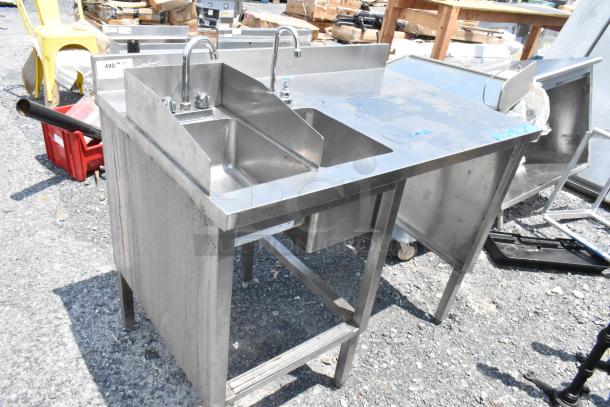 Stainless steel table with two single sink bays, faucets, and handles. Used condition, suitable for commercial kitchen use.