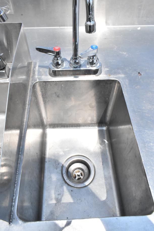 Stainless steel table with two single sink bays, visible faucets, and handles; minor surface wear.