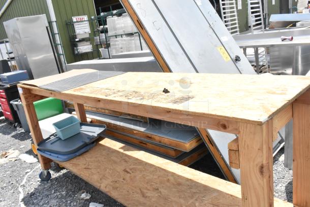 Wooden table with under shelf, features commercial casters for mobility. Slightly worn top; ideal for workshop use.