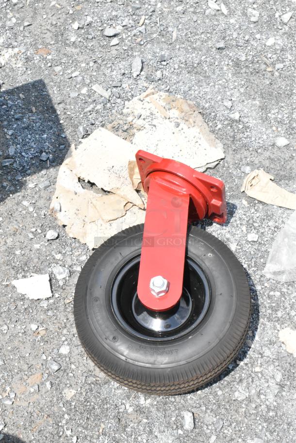 Red caster wheel with mounting bracket on gravel, surrounded by cardboard pieces.