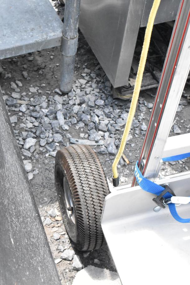 Filmtools metal furniture dolly with rubber tires, sturdy metal frame, and securing straps, shown in an outdoor setting.