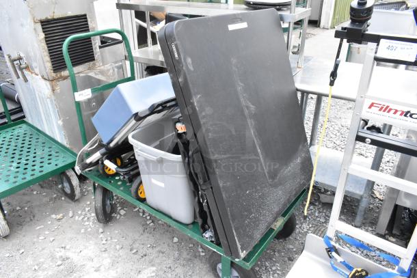 Green metal flat cart with folding table, poly bin, and miscellaneous contents. Cart is sturdy with some wear visible.